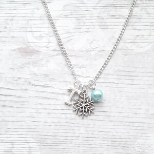 May include: Silver necklace with a snowflake charm, a letter 'T' charm, and a light blue pearl.