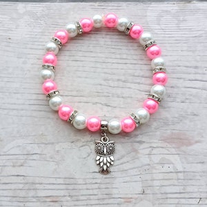 May include: A pink and white beaded bracelet with a silver owl charm. The beads are alternating pink and white with clear rhinestones.