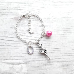 May include: Silver charm bracelet with a ballerina charm, a pink bead, a star, and the number 0 charm. The bracelet is displayed on a white wooden surface.