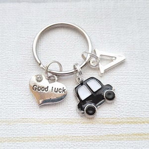 May include: A silver key ring with a black car charm, a heart charm with the words "Good Luck" and a silver charm with the letter "A".