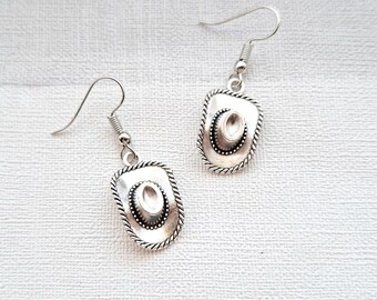 May include: A pair of silver dangle earrings featuring a cowboy hat design. The hats are detailed with a textured rim and a small, round center.