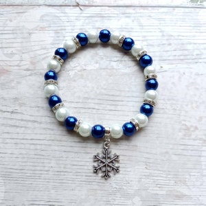 May include: A bracelet with white and deep blue beads, interspersed with silver spacers and a snowflake pendant. The round beads are strung together to form a wrist accessory. The bracelet is a winter-themed piece.