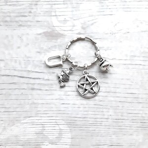 May include: Silver keychain with a pentagram charm, a witch charm, a cauldron charm, and a letter U charm.