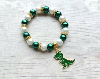 May include: A green and white beaded bracelet with a gold dinosaur charm. The beads are alternating green and white with gold accents.