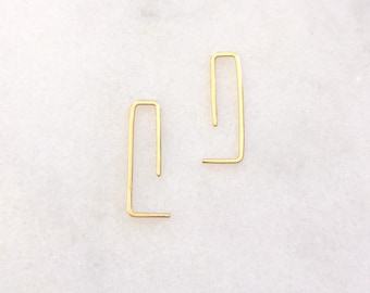 May include: A pair of gold-toned minimalist earrings with a simple geometric design. Each earring is a thin, open rectangle with a slight bend in the middle.