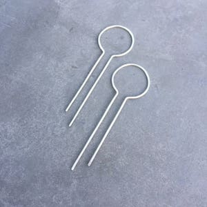 May include: Two silver hair pins with a circular loop at the top. The pins are straight and have a smooth finish.