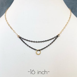 May include: A delicate necklace with a two-tiered chain design. The top chain is gold-colored, transitioning to a black chain below. A small gold-colored circle pendant hangs from the bottom chain. The necklace is approximately 16 inches long.