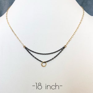 May include: A two-tone necklace with a gold chain and a black chain design. The necklace has two layers of black chain with a gold circle pendant. The necklace is approximately 18 inches long.