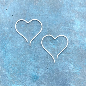 May include: Two silver-toned heart-shaped wire earrings. Each earring is formed from a single continuous piece of thin metal wire, bent into an open heart outline with a small gap at the bottom point, creating a simple and clean aesthetic.
