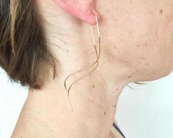 May include: A pair of long, gold, wire earrings with a wavy, abstract design.