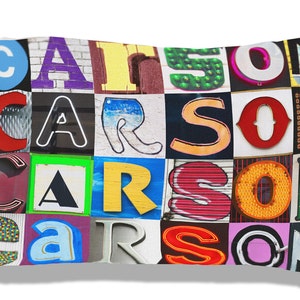 Puede incluir: Una almohada blanca con el nombre "CARSON" escrito en letras de colores. Cada letra está compuesta por una imagen diferente, como una señal de tráfico, un letrero de neón o una fachada de edificio.