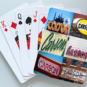 Puede incluir: Un primer plano de una mano de cartas de juego, incluyendo el As de Picas, el Rey de Diamantes, la Reina de Picas, el Jack de Diamantes y el 10 de Diamantes. Las cartas están abiertas en abanico y están delante de un collage de imágenes con la palabra "Carson" en varios colores y tipos de letra.