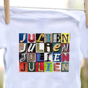 May include: White baby onesie with a colorful graphic of the name "Julien" spelled out in different fonts and colors.