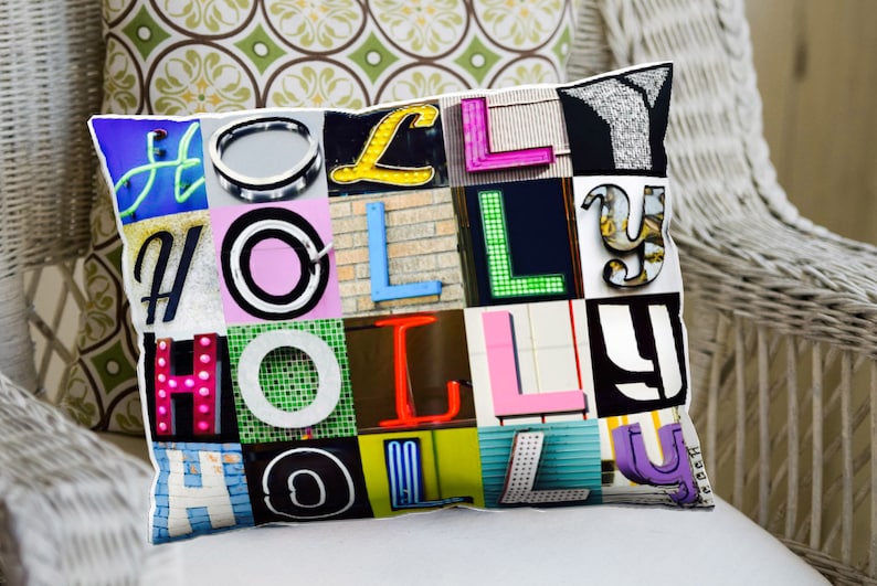 Op de afbeelding: Een decoratief kussen met een kleurrijk patchwork-ontwerp met het woord "HOLLY" gespeld in verschillende lettertypen en kleuren. De letters zijn gemaakt van verschillende materialen, waaronder metaal, plastic en neon.