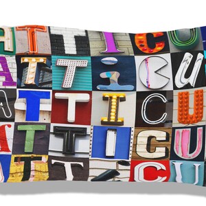 Könnte beinhalten: Ein weißes Kissen mit dem Namen "ATTICUS", der in bunten Buchstaben geschrieben ist. Jeder Buchstabe besteht aus einer Collage verschiedener Bilder.