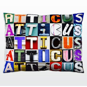 Könnte beinhalten: Ein Kissen mit dem Namen "Atticus", der in bunten, vintage-artigen Buchstaben geschrieben ist. Jeder Buchstabe hat eine andere Farbe und einen anderen Stil, was ein einzigartiges und auffälliges Design ergibt.