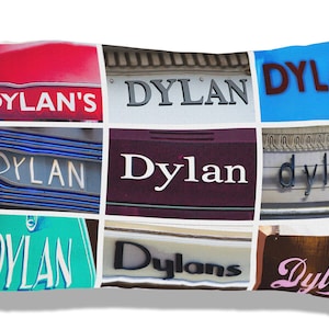 May include: A decorative pillow featuring a collage of signs with the name "Dylan" in various fonts and colors. The signs include red, blue, and green backgrounds, with the name in white, black, and brown. The pillow is rectangular and white.