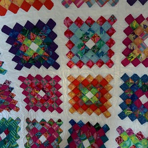 May include: A colorful quilt with a white background and a pattern of squares made from different fabrics. Each square is made up of smaller squares in a variety of colors and patterns.