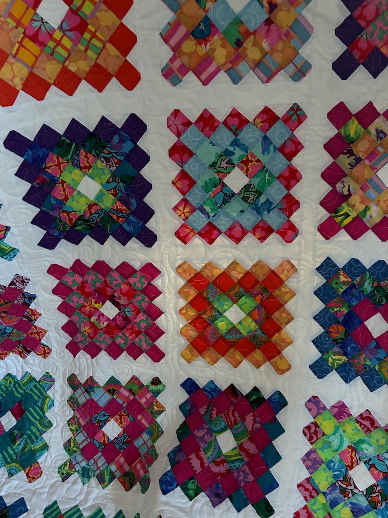 May include: A colorful quilt with a white background and a pattern of squares made from different fabrics. Each square is made up of smaller squares in a variety of colors and patterns.