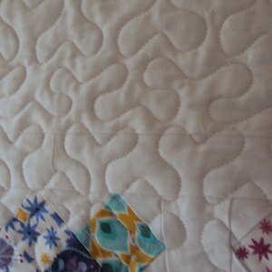 May include: White quilted fabric with a wavy pattern. The fabric is bordered with colorful patchwork squares in shades of pink, blue, green, and yellow.