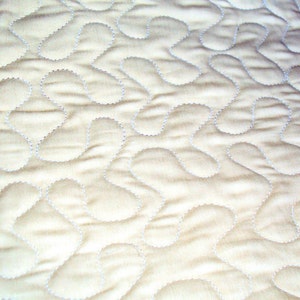 May include: A close-up of a white quilted fabric with a pattern of small, curved lines. The fabric has a soft, textured surface.