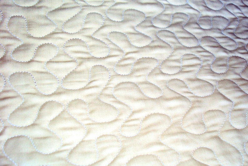 May include: A close-up of a white quilted fabric with a pattern of small, curved lines. The fabric has a soft, textured surface.