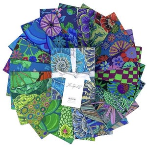 Può includere: Una collezione di quadrati di tessuto in varie tonalità di blu, verde, viola e rosso, disposti a cerchio. I tessuti presentano disegni floreali e astratti, con un fascio centrale legato con un nastro bianco e un'etichetta "Free Spirit".