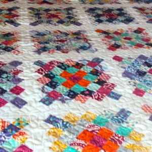 May include: A white quilt with a patchwork design featuring squares of various colors and patterns, including blue, purple, orange, and red.