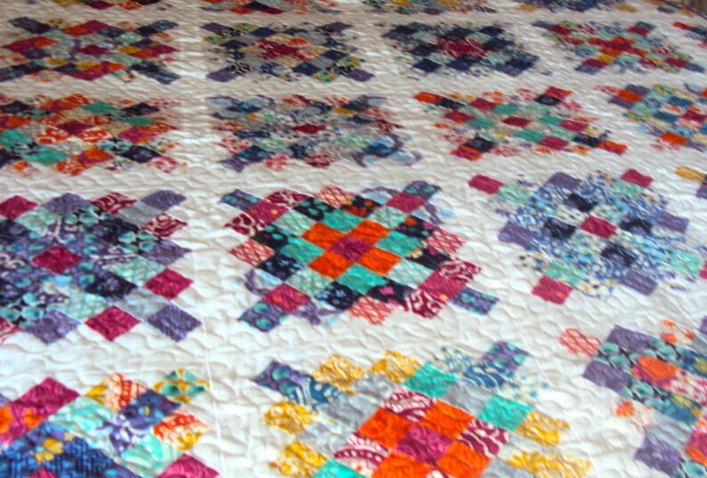 May include: A white quilt with a patchwork design featuring squares of various colors and patterns, including blue, purple, orange, and red.