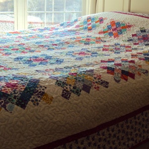 May include: A white quilt with a patchwork design featuring a variety of colors, including pink, blue, green, and yellow. The quilt is made with a variety of fabrics and patterns, and it is quilted with a simple stitch.