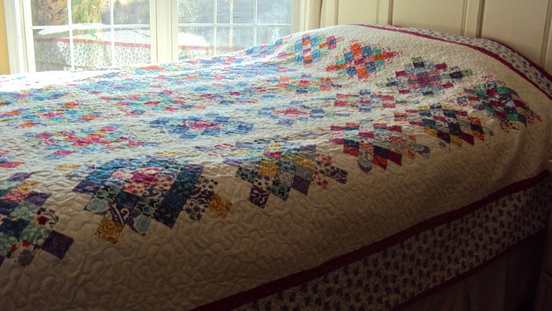May include: A white quilt with a patchwork design featuring a variety of colors, including pink, blue, green, and yellow. The quilt is made with a variety of fabrics and patterns, and it is quilted with a simple stitch.