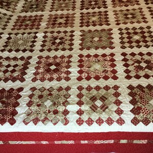 Puede incluir: Un edred&oacute;n hecho a mano con un patr&oacute;n repetido de bloques cuadrados en tonos de rojo, crema y beige. Los bloques est&aacute;n dispuestos en una cuadr&iacute;cula, con un borde rojo en la parte inferior. El edred&oacute;n probablemente est&aacute; hecho de algod&oacute;n.