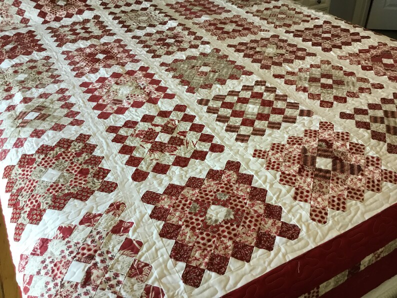 Puede incluir: Un edred&oacute;n hecho a mano con un patr&oacute;n repetitivo de formas de diamante rojas y blancas. El edred&oacute;n presenta varios tonos de telas rojas y blancas, creando un dise&ntilde;o texturizado y visualmente atractivo. Un art&iacute;culo de cama acogedor y decorativo.