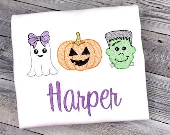 May include: White t-shirt featuring embroidered Halloween designs: a ghost with a purple bow, an orange pumpkin, and a green Frankenstein's monster. The name "Harper" is embroidered in purple script below the designs.