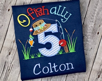 May include: Navy blue t-shirt with embroidered fishing-themed design. Features the text "Fish ally" and the name "Colton" below a large number 5 with a fishing rod, bobber, and fish. Includes a fishing hat and grass.