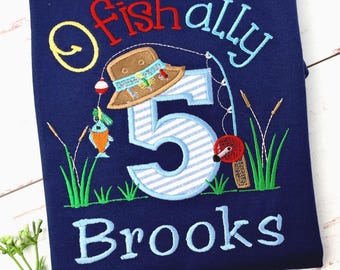 May include: A navy blue t-shirt featuring an embroidered design with the text "Fish ally" in red and light blue, a brown fishing hat, a large number 5 with light blue stripes, a fishing rod, and the name "Brooks" in light blue.