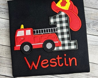 May include: Black t-shirt with a red fire truck, a black and white checkered number one, and a red firefighter hat. The name "Westin" is embroidered in red below the design.