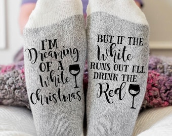 May include: A pair of heather gray socks with white cuffs featuring black text. The left sock reads I'M Dreaming OF A white Christmas with a wine glass icon. The right sock reads BUT IF THE white RUNS OUT I'LL DRINK THE Red with a wine glass icon.