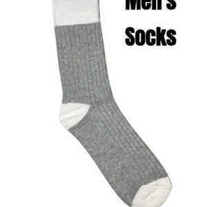May include: A ribbed crew sock featuring a grey body with a white heel and toe. The cuff is white with a single horizontal black stripe at the top. The text "Men's Socks" is printed in black to the right of the sock against a plain white background.