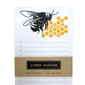 May include: A notepad with a black and white bee illustration and a honeycomb design with the word "honey" spelled out in yellow. The notepad is brown and has the text "LYNN-OLEUM NOTEPAD 50 sheets" printed on it.