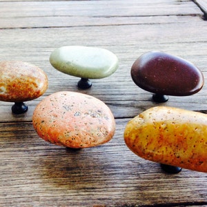 Può includere: Cinque tiretti per cassetti in pietra naturale di diversi colori e forme. I tiretti sono montati su una superficie in legno.