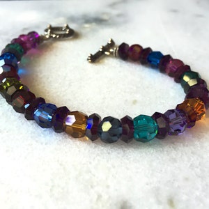 May include: A multi-coloured crystal bracelet with a silver clasp. The bracelet features a rainbow of colours including purple, blue, green, and amber.