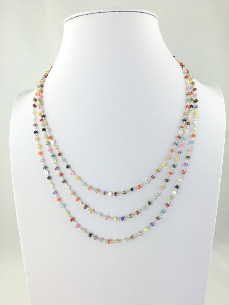 May include: A multi-strand necklace with small, colorful gemstone beads. The necklace is made of silver and features a variety of colors, including red, orange, yellow, green, blue, purple, and pink.