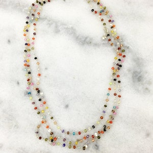 May include: A multi-strand necklace with small, colorful gemstone beads. The necklace is made of silver chain and features a variety of colors, including red, orange, yellow, green, blue, purple, and pink.