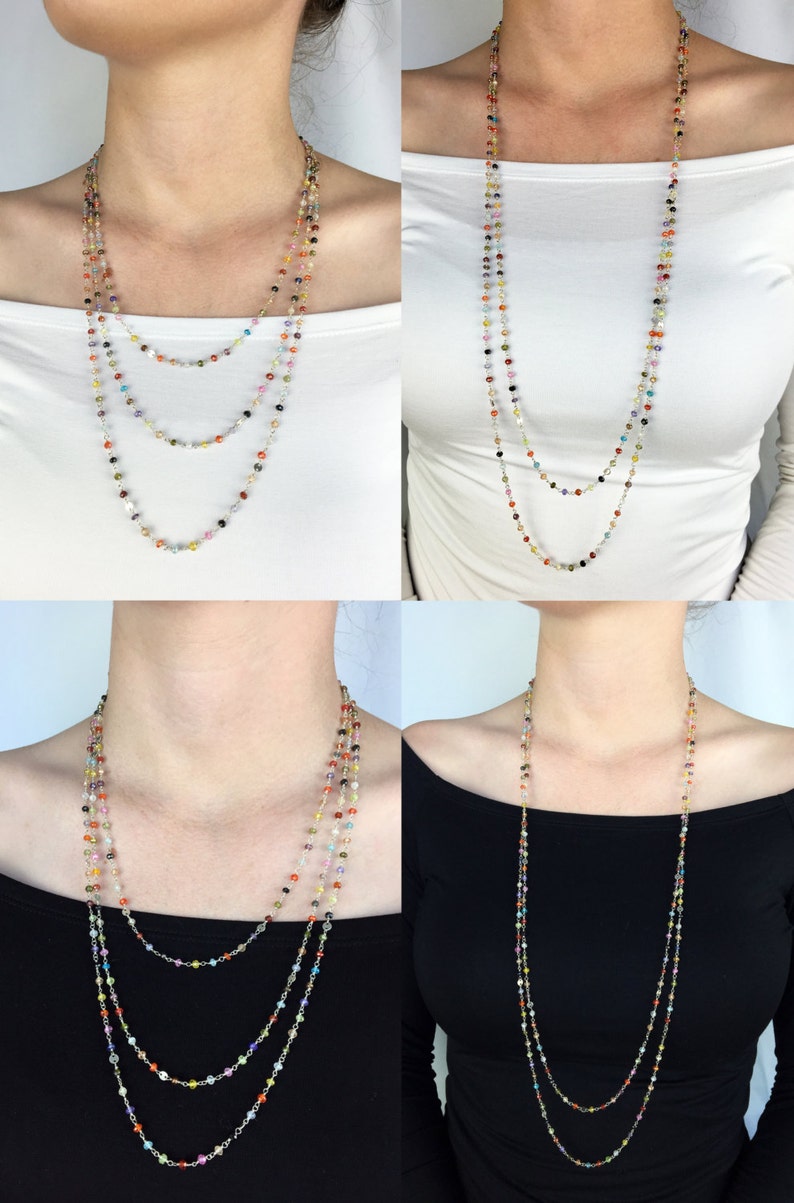 May include: A multi-strand necklace with small, colorful beads. The necklace is layered and features a variety of colors, including red, orange, yellow, green, blue, purple, and pink. The necklace is shown on a model wearing a white shirt and a black shirt.