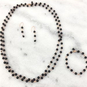 May include: A set of black onyx jewelry featuring a necklace, earrings, and a bracelet. The jewelry is made with rose gold accents.