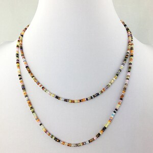 Può includere: Una collana di perline multicolori con una varietà di perline di pietre preziose in tonalità di marrone, verde, giallo, arancione, rosa e viola. La collana è a strati e sembra essere fatta di piccole perline rotonde.