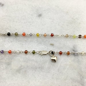 May include: A silver chain necklace with a heart charm. The chain is adorned with small, colorful beads in shades of red, orange, yellow, green, blue, and purple.