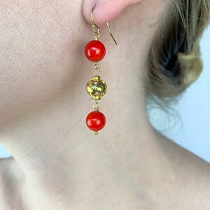 May include: Gold dangle earrings with three beads. The top and bottom beads are red, and the middle bead is gold with a decorative design.