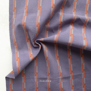 May include: A close-up of a folded fabric with vertical stripes. The fabric is a muted purple color with orange and gray stripes. The word "FABLEISM" is printed in white on the lower right corner.